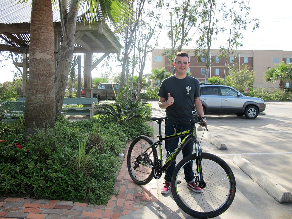 UAG resident standing with a bicycle beneath the trees